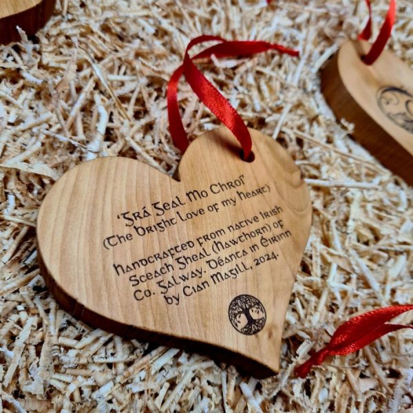 Wooden love heart decoration engraved with text that reads "Handcrafted in County Galway from local Irish wood by Cian Magill", with red ribbon attached.